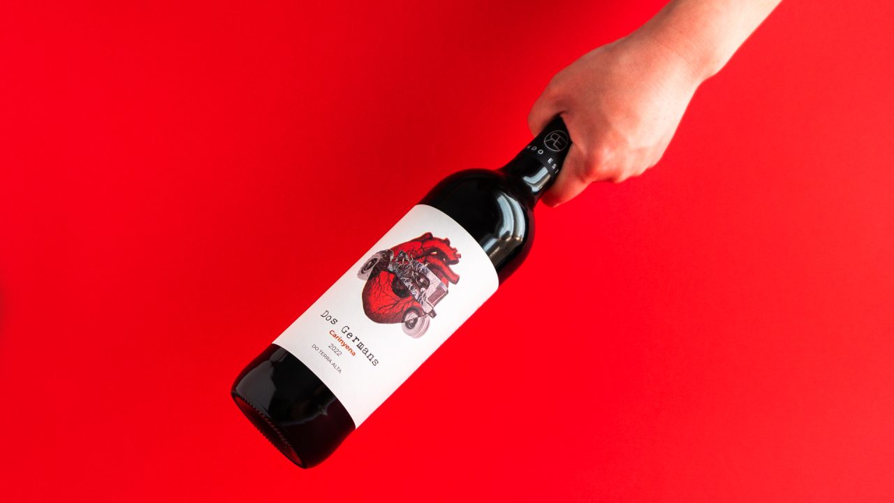 Ampolla de vi negre agafada d'una mà sobre fons roig