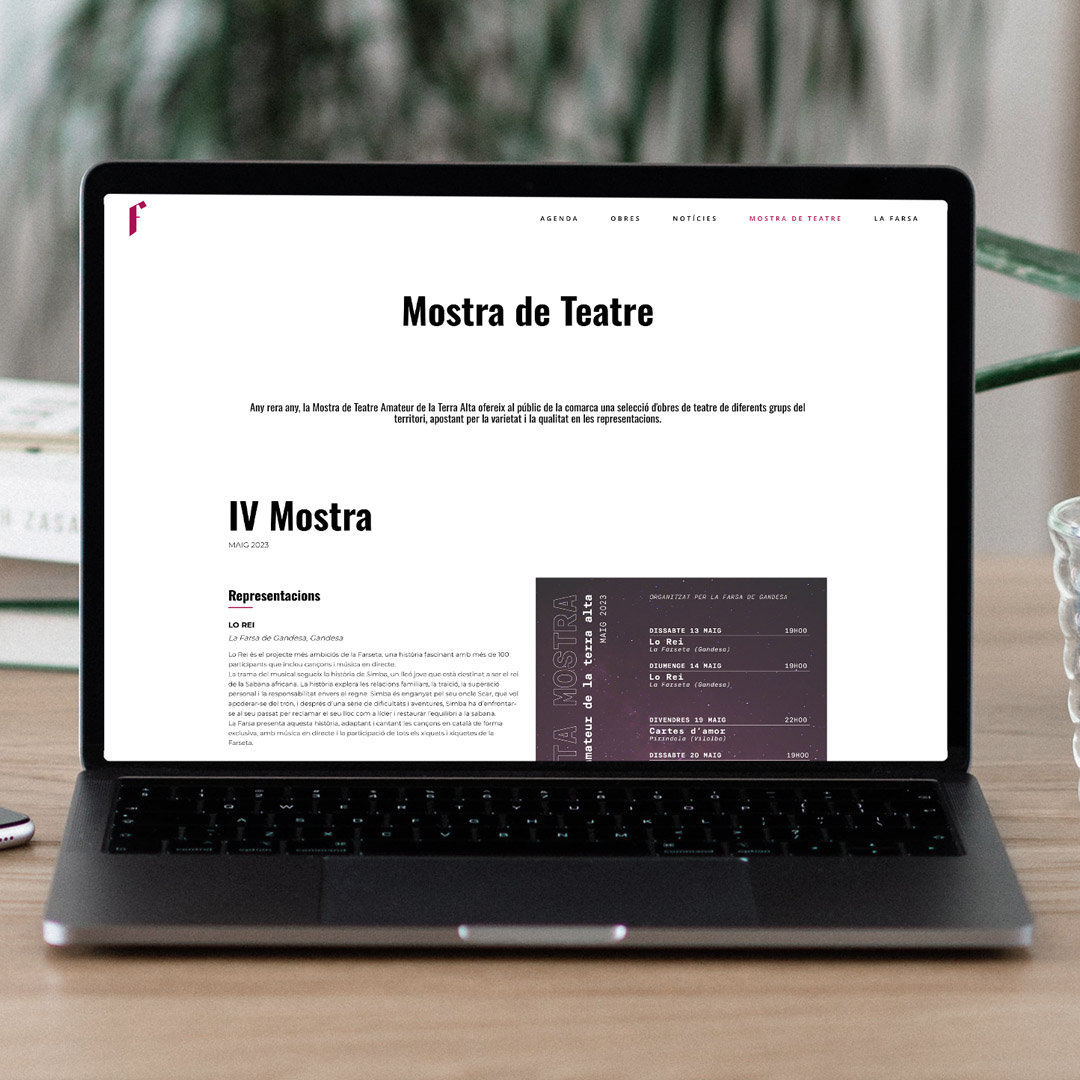 Macbook amb la pàgina web de La Farsa oberta sobre una taula de fusta i amb una planta al fons