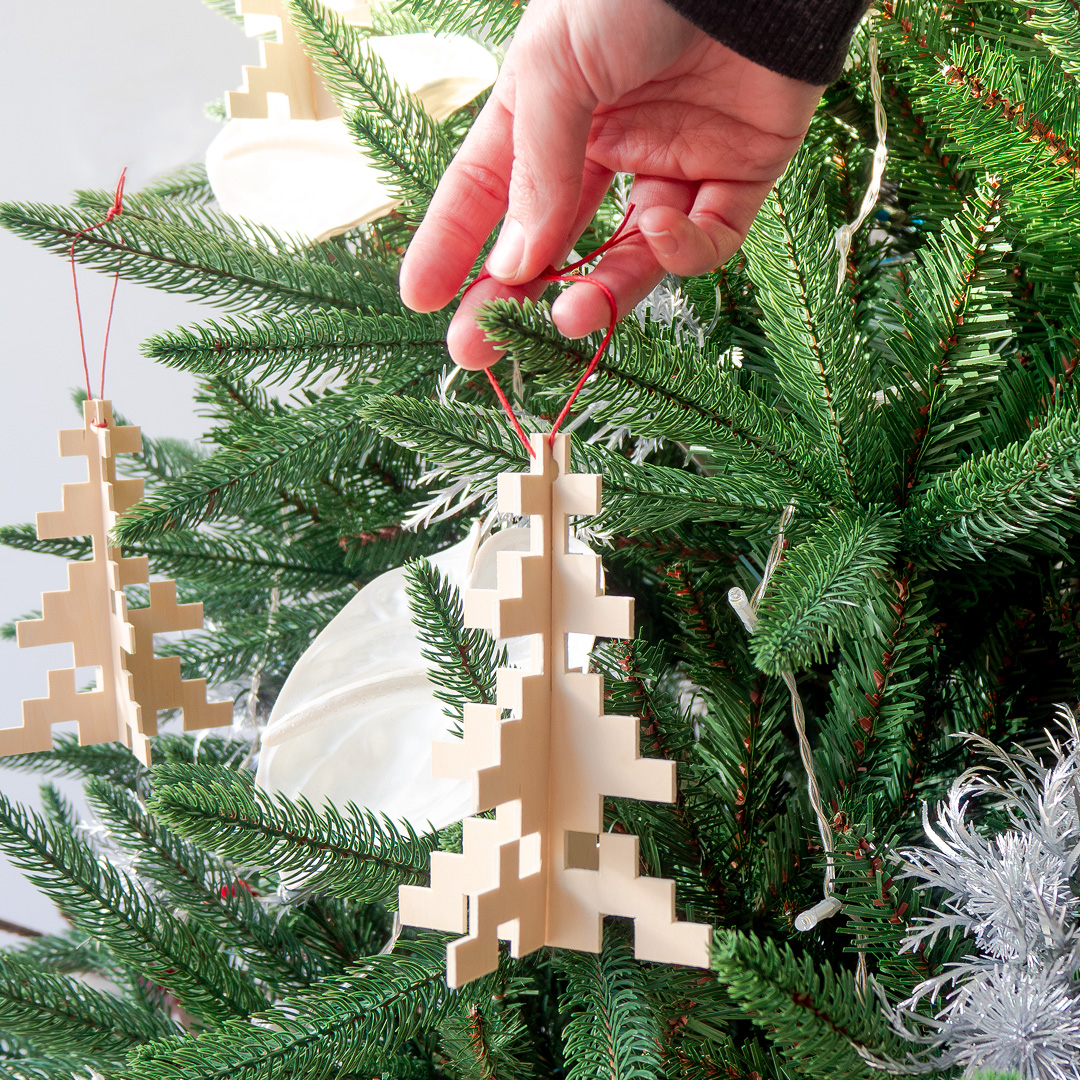 Mà que col·loca un ornament de nadal en forma de arbre penjat a un arbre de Nadal amb decoracions de color blanc i platejades