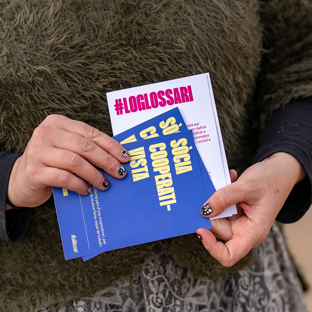 Detall dels targetons A6 del Glossari del Cooperativisme agafats per unes mans