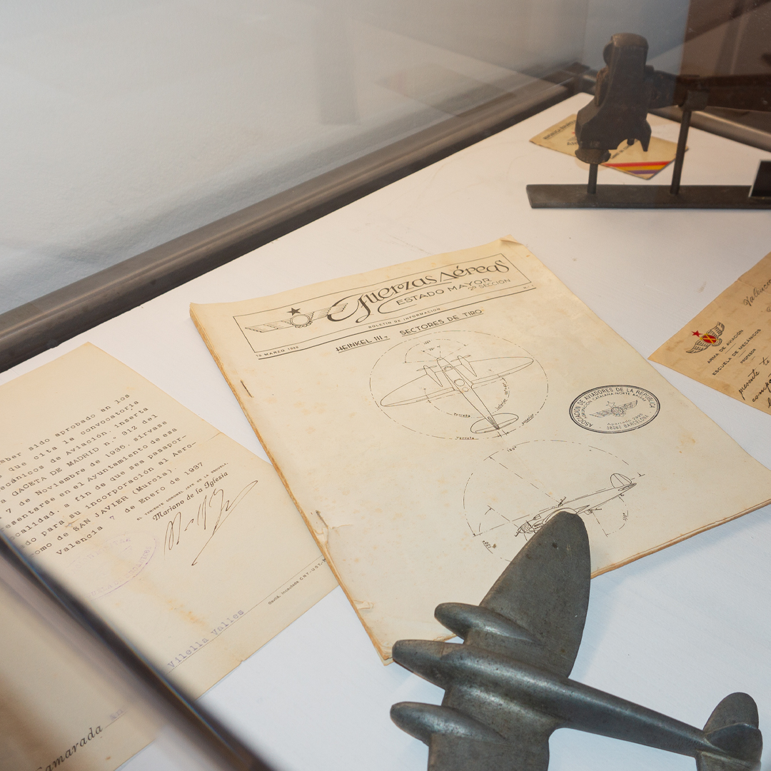 Detall de documents antics sobre una vitrina i un avió metàlic